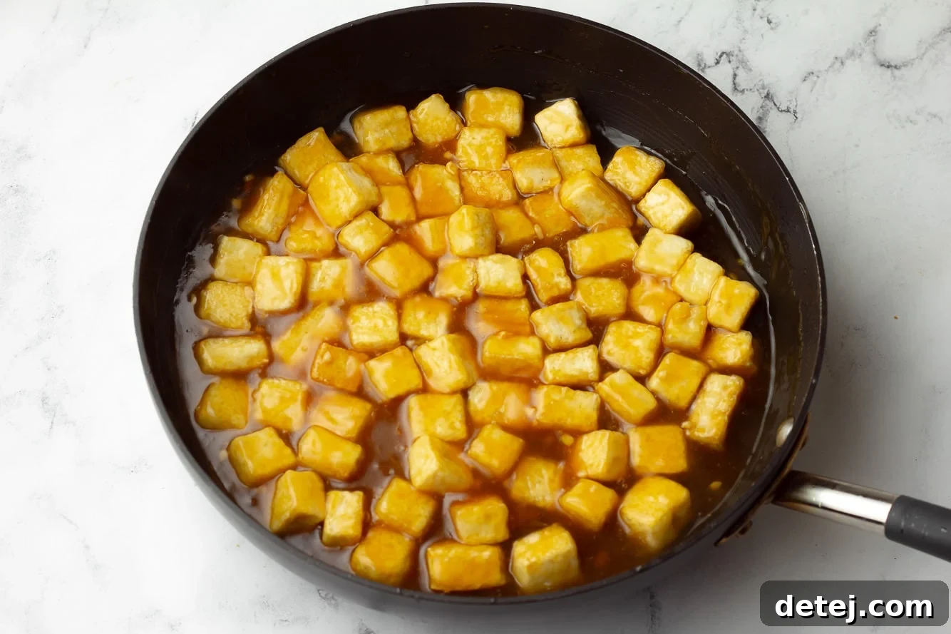Crispy baked tofu cubes coated in a vibrant orange sauce in a black skillet, ready to be served.