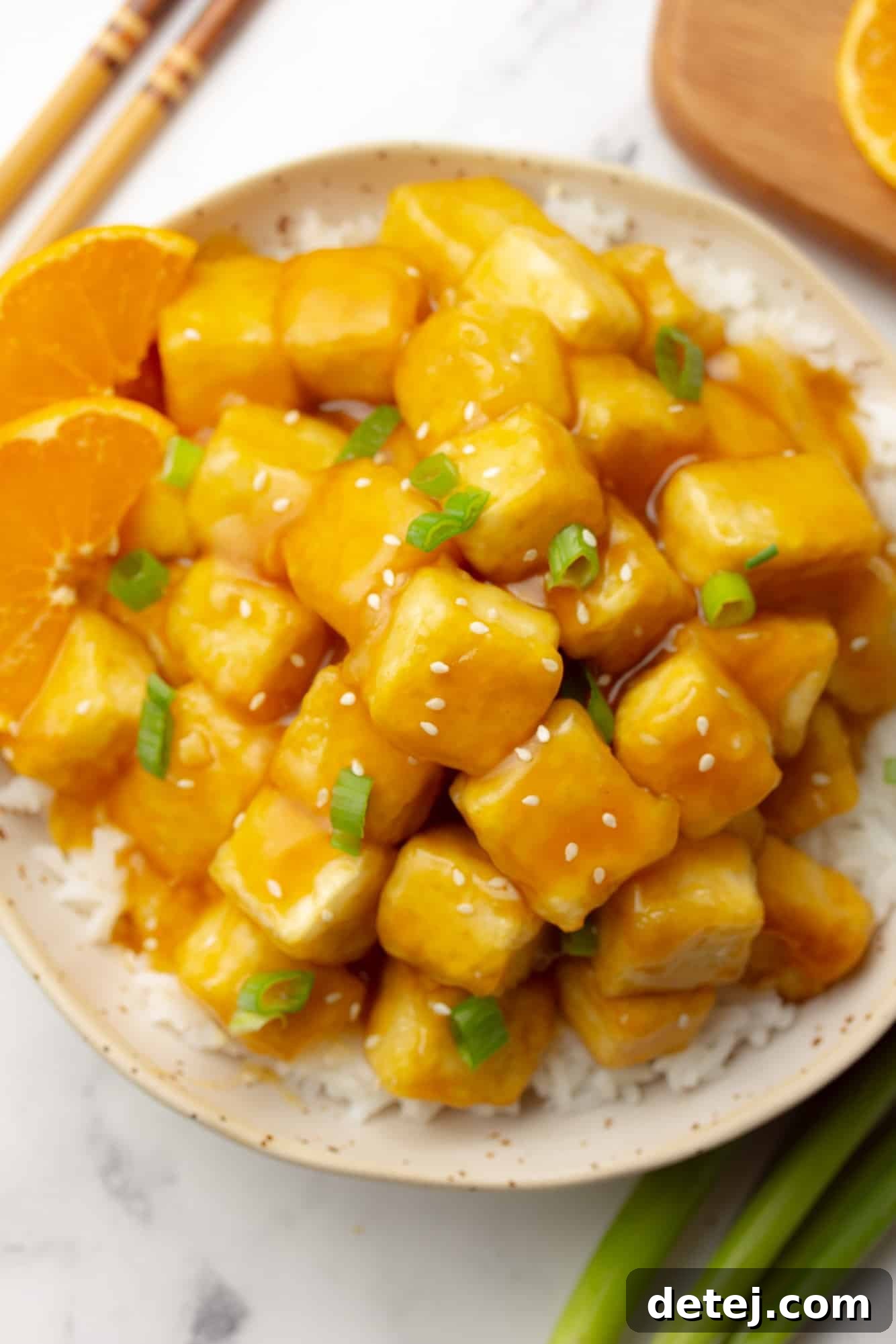 Delicious vegan orange tofu served over a bed of white rice in a bowl, garnished with green onions and orange slices.