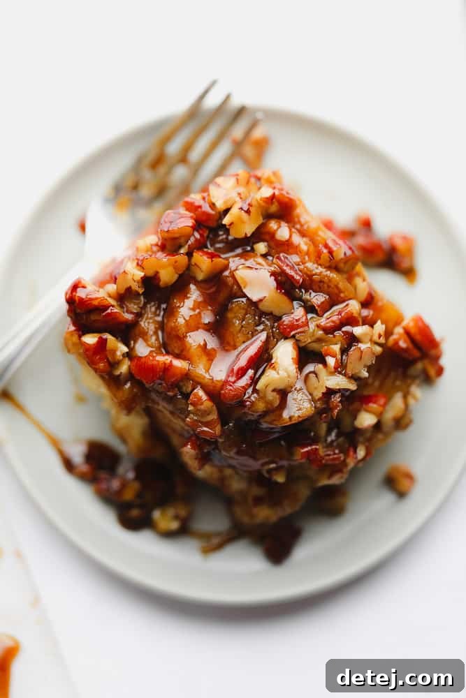A perfectly baked sticky bun adorned with rich caramel and crunchy pecans, resting elegantly on a white plate with a fork beside it, against a pristine white background.