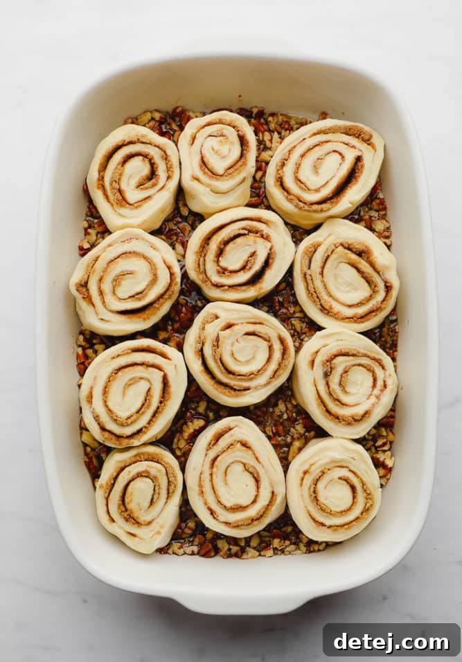 Unbaked sticky buns carefully arranged in a casserole dish, topped with a generous layer of caramel sauce and pecans, ready for baking.