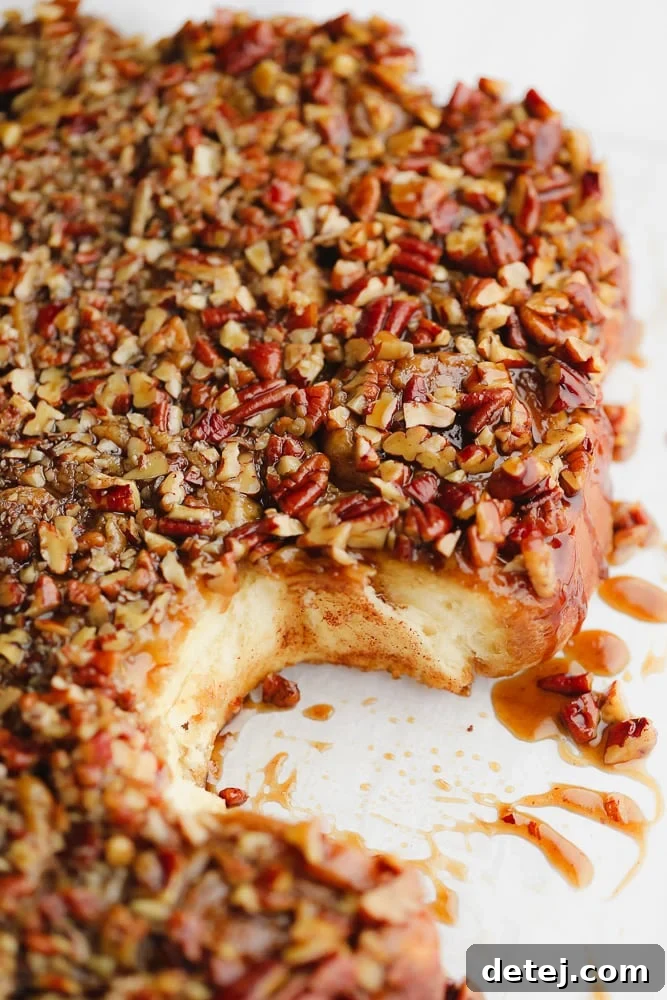 A close-up shot of perfectly golden-brown sticky buns, freshly baked and glistening with a thick layer of gooey caramel and toasted pecans.