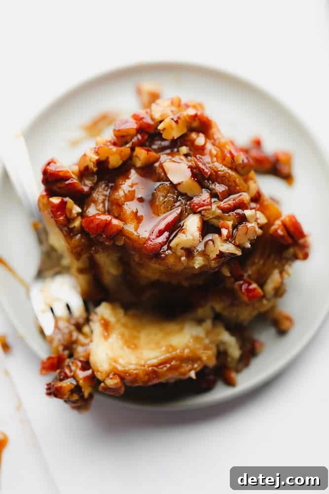 A close-up of a sticky bun with a bite taken out, revealing the soft, cinnamon-swirled interior and the gooey caramel pecan topping.