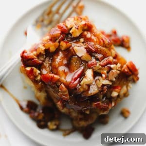 A square image of a perfectly baked sticky roll with a glossy caramel pecan topping, served on a white plate.