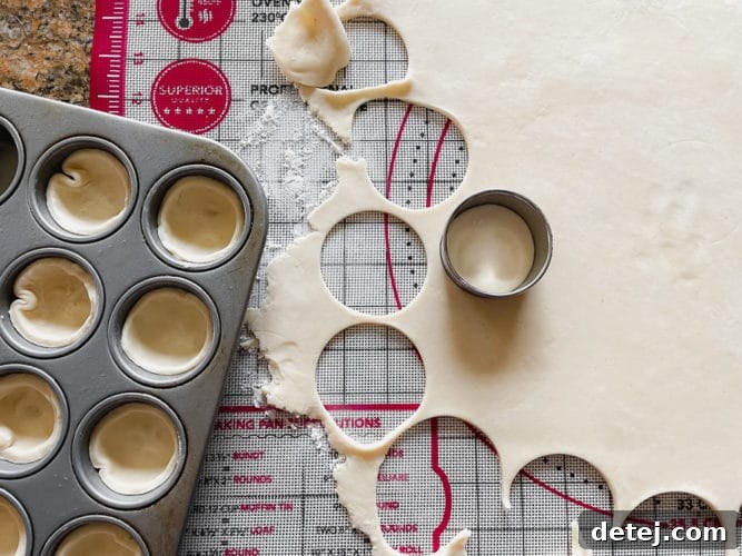Close-up shot of vegan pie crust dough being rolled out on a patterned pastry mat, with several small, perfect circles already cut out using a round cookie cutter, preparing for mini pies.