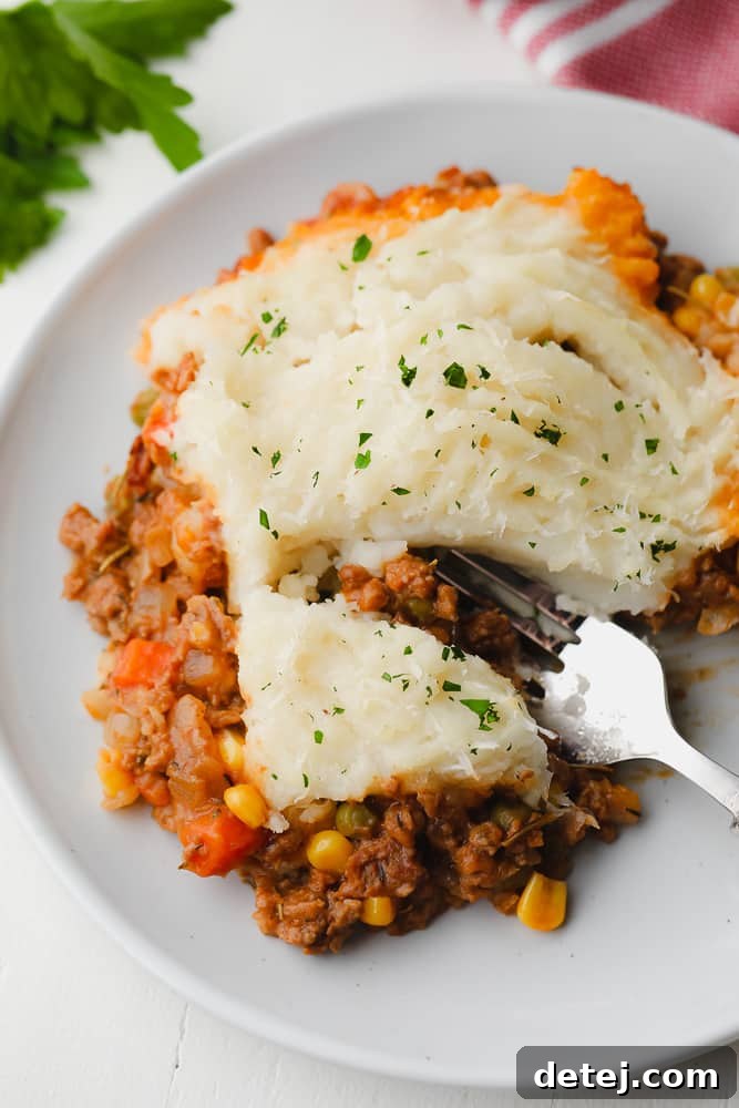 close up of a fork taking a bite out of a meaty pie with potatoes on top