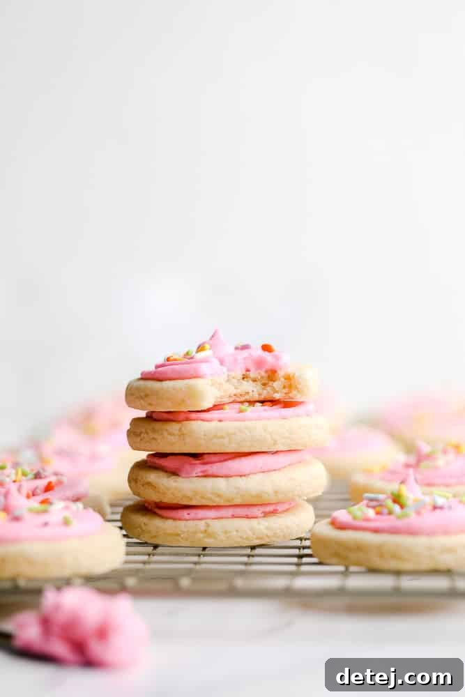 A stack of four perfectly pink-frosted vegan Lofthouse cookies, adorned with colorful sprinkles.