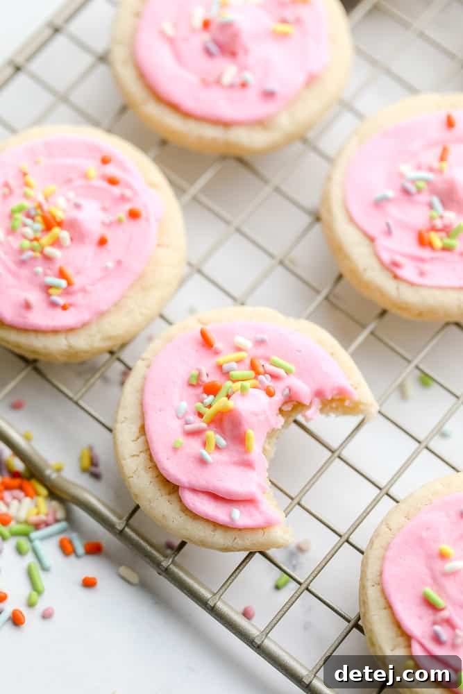 A cooling rack filled with many frosted vegan Lofthouse cookies, one with a bite taken out, showing its soft interior and vibrant sprinkles.