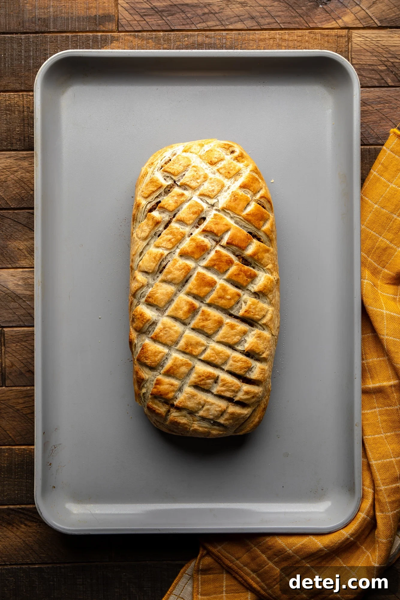 Overhead view of a perfectly baked, golden-brown vegan wellington on a baking sheet, fresh out of the oven.