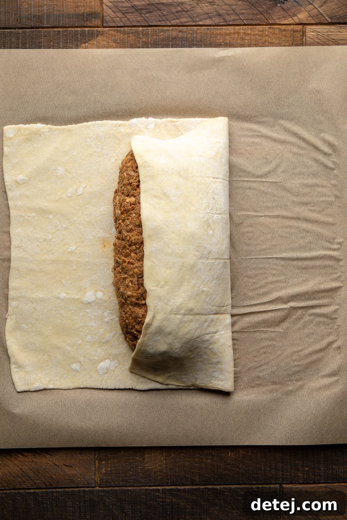 A partially assembled pastry-wrapped vegan wellington on parchment paper, showing the first fold.
