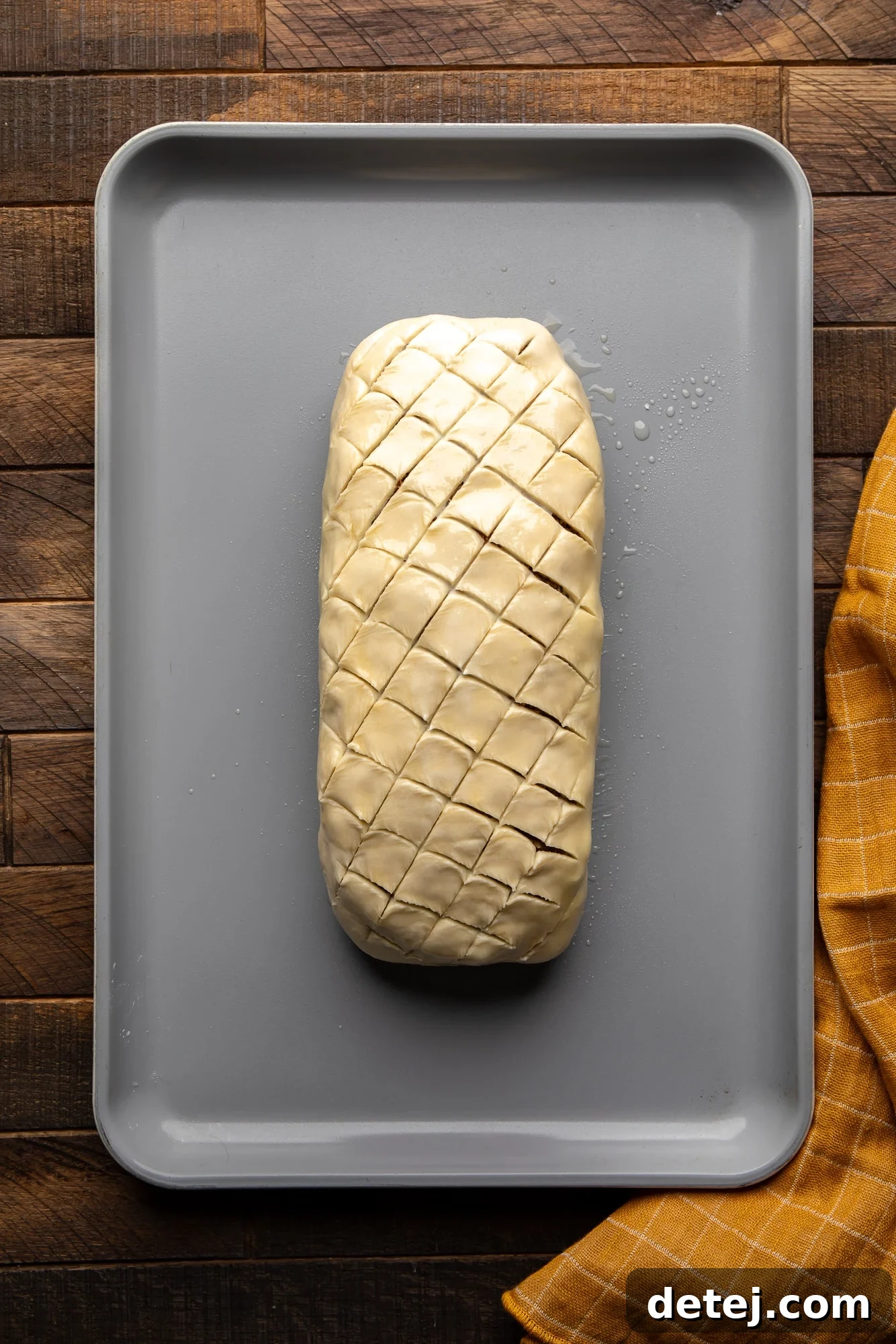 Overhead view of a beautifully scored, unbaked vegan wellington on a baking sheet, ready for the oven.