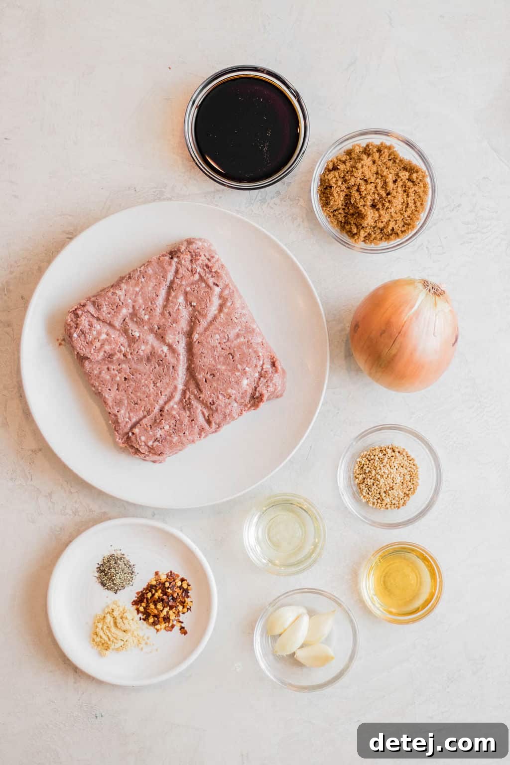 raw vegan beef on a white plate next to small bowls of sauces, seasonings, onion, and brown sugar.