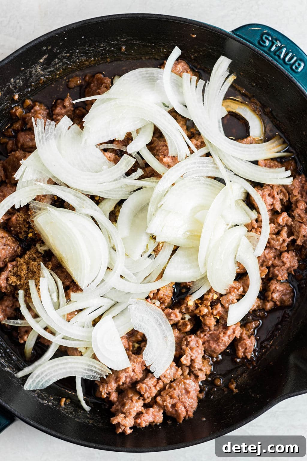 raw onions on top of cooked vegan ground beef in a black skillet.