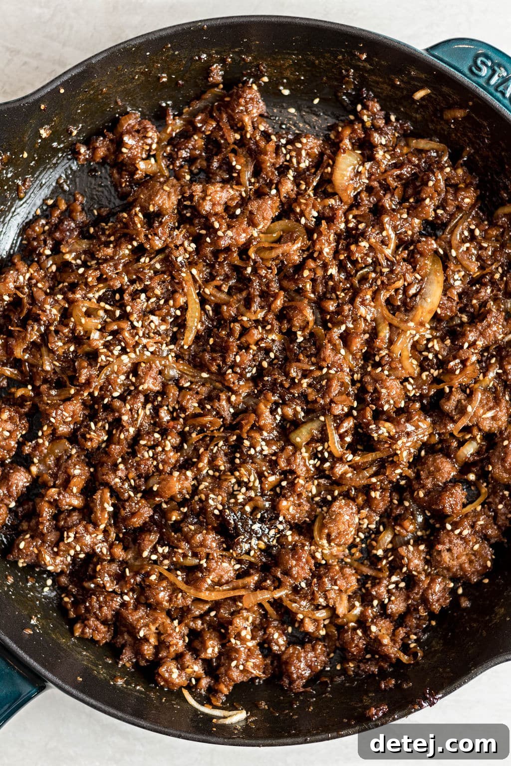 cooked vegan ground beef and onions covered in sesame seeds in a black skillet.