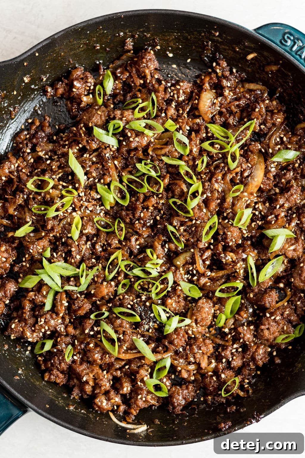 cooked vegan ground beef and onions covered in green onions in a black skillet.