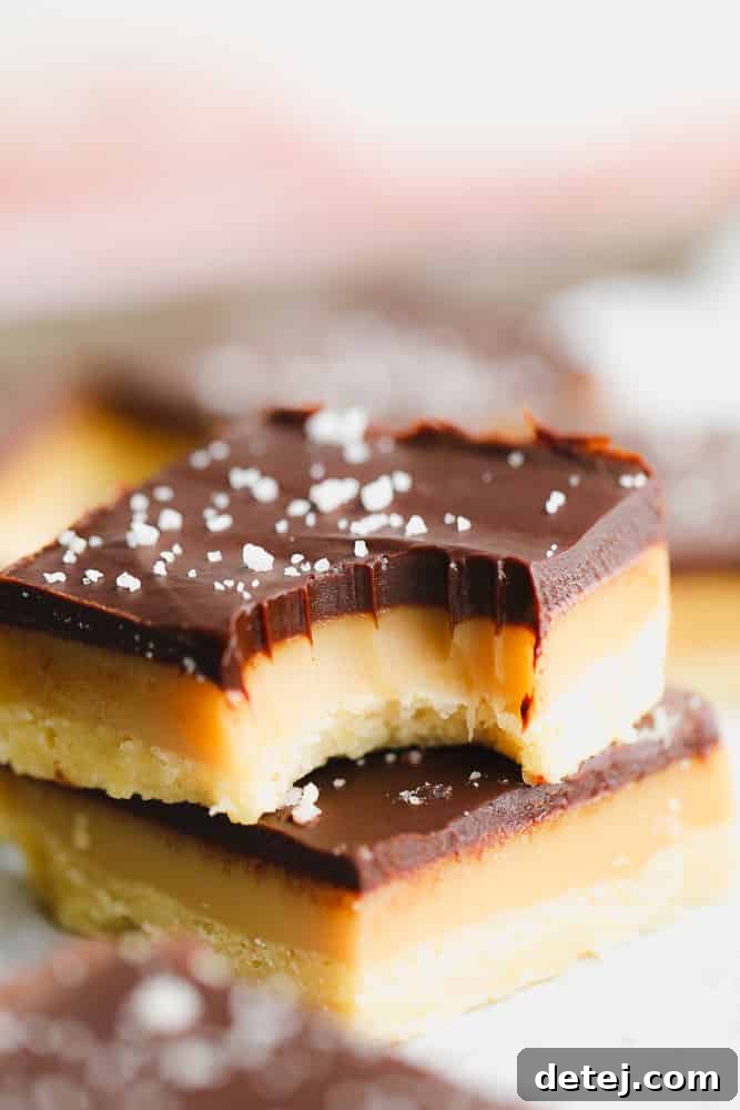 A close-up view of a perfectly layered Vegan Millionaire Shortbread bar with a bite taken out, revealing the distinct shortbread, caramel, and chocolate layers.