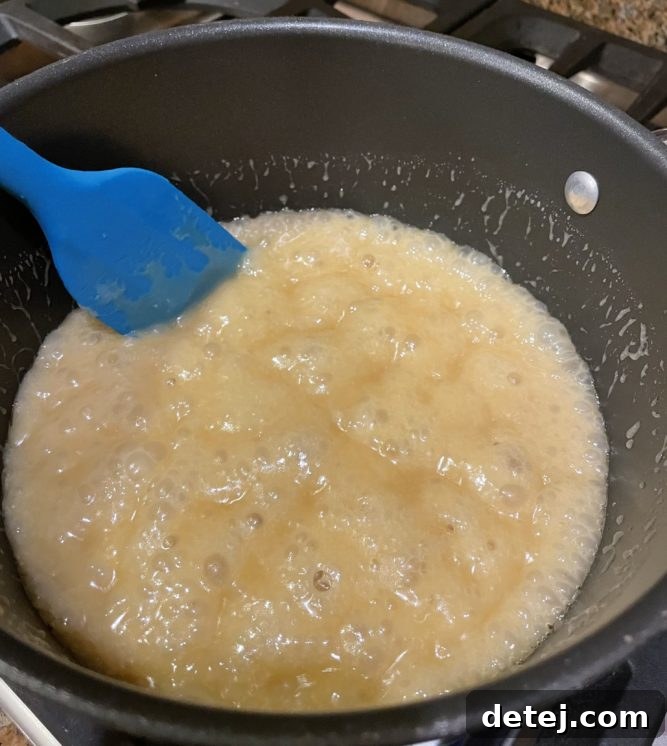 Close-up of golden caramel bubbling gently in a saucepan over heat.