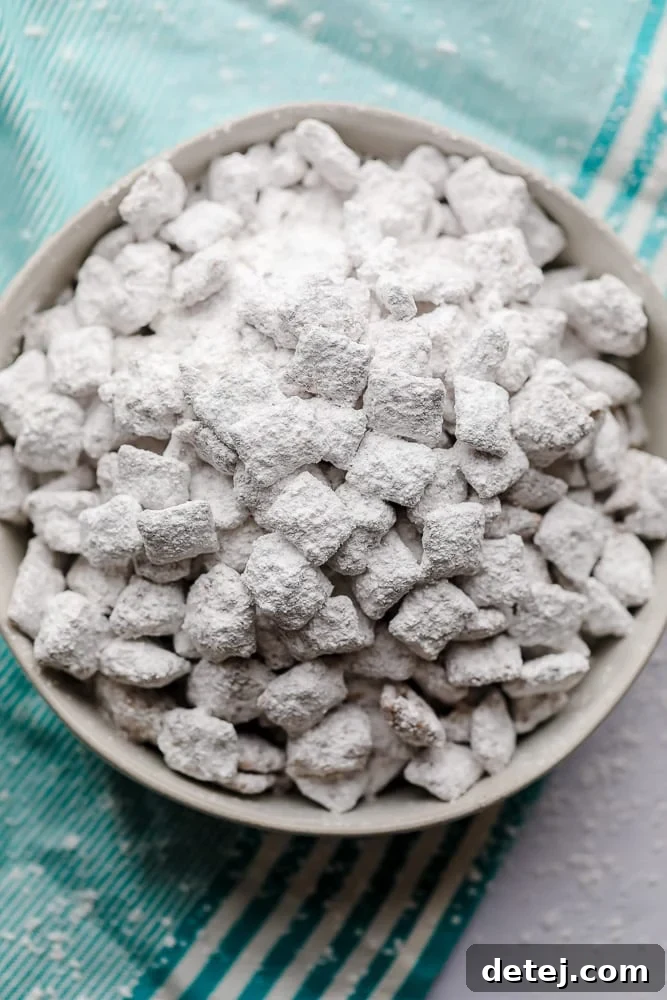 A top-down view of a bowl filled with perfectly coated vegan muddy buddies, resting on a stylish blue striped towel. A delightful, easy-to-make, no-bake vegan dessert that's perfect for snacking and special occasions.