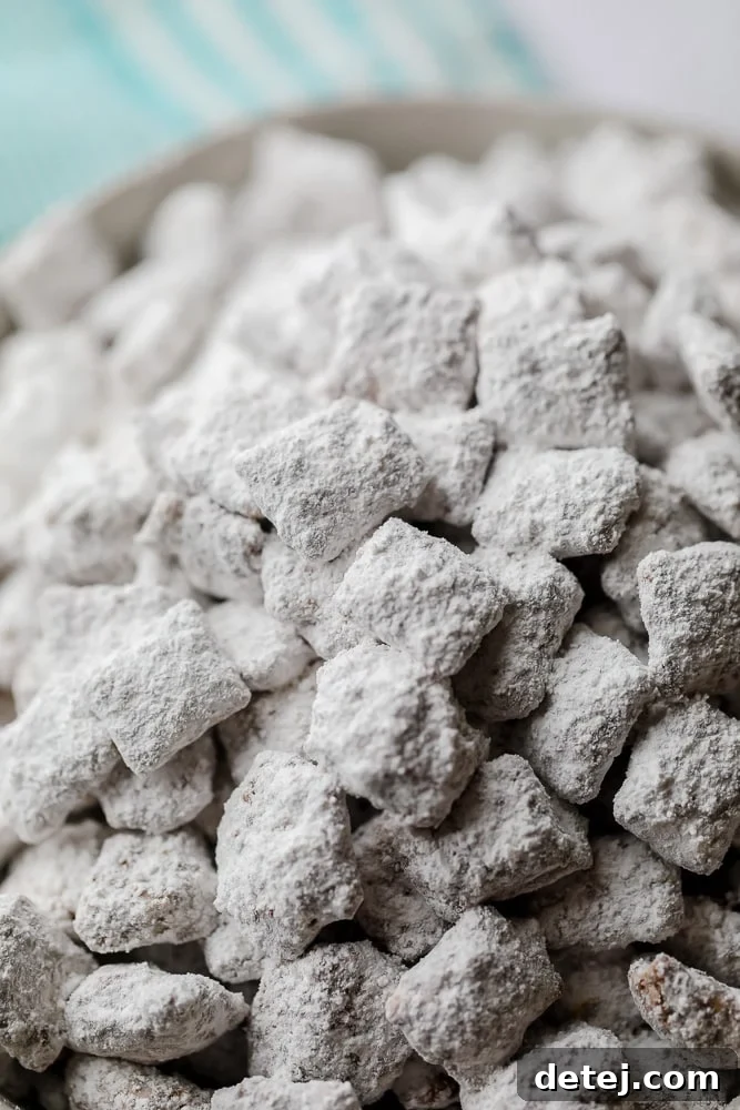A close-up shot of rice Chex cereal generously coated with powdered sugar, showcasing the classic white finish of muddy buddies. This irresistible texture is what makes the snack so delightful.