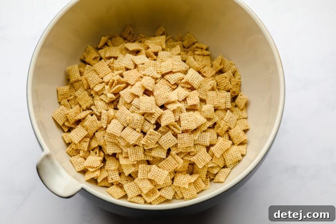 A large bowl filled with rice Chex cereal, ready for the next steps in making vegan muddy buddies. The foundation of this delicious, crunchy snack.