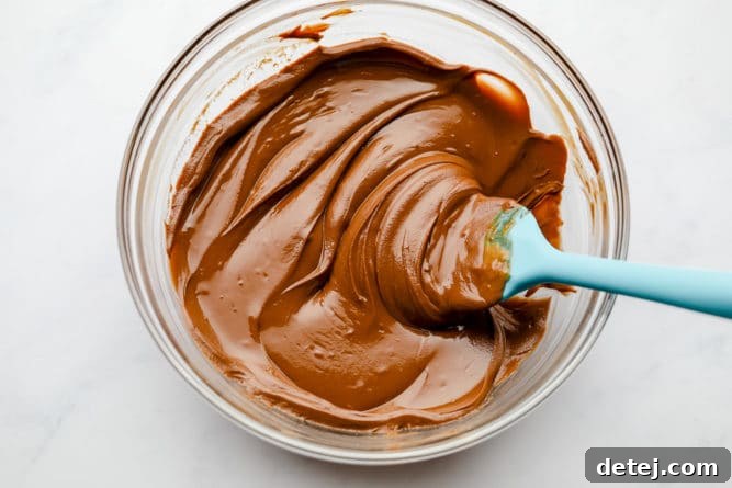 A rich, glossy melted chocolate and peanut butter mixture in a bowl, perfectly smooth and creamy, ready to coat the cereal. The irresistible base of vegan muddy buddies.
