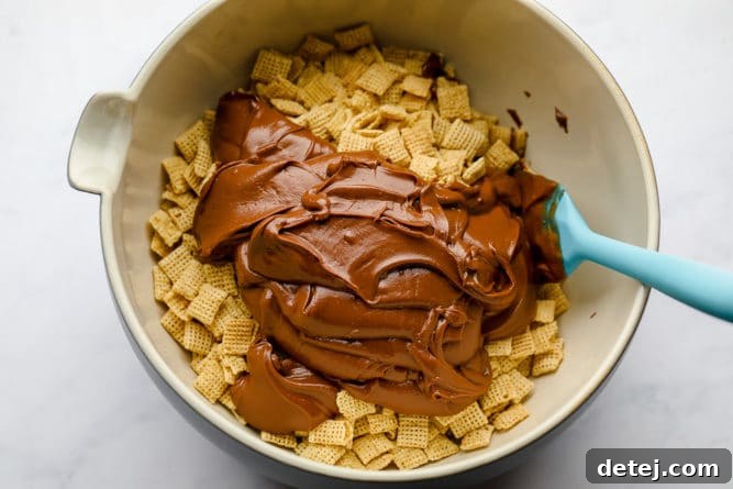 Melted chocolate and peanut butter mixture drizzled over rice Chex cereal in a large bowl, before mixing, showcasing the rich coating.