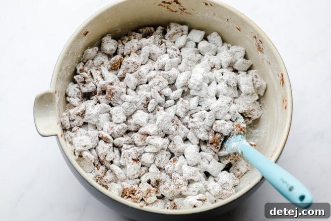 A spatula gently mixing chocolate and powdered sugar with cereal in a bowl, showcasing the process of coating the vegan muddy buddies to perfection.