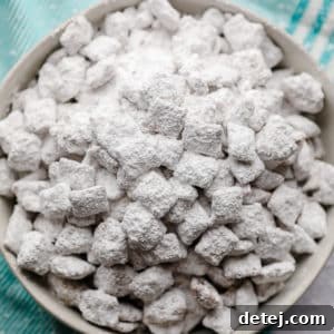A square image of a bowl of perfectly coated vegan muddy buddies with powdered sugar.