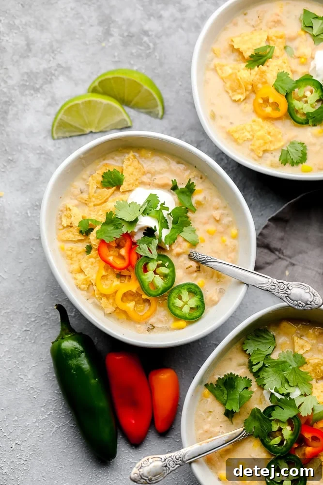 Three bowls of creamy vegan white chili, garnished with fresh herbs and toppings, on a rustic grey background.