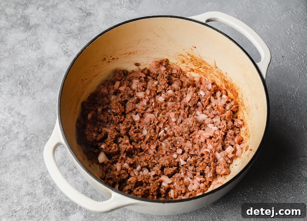 Ultimate Plant-Based Spaghetti 4 Sautéing vegan ground beef and diced onions in a large white pot until browned and translucent.