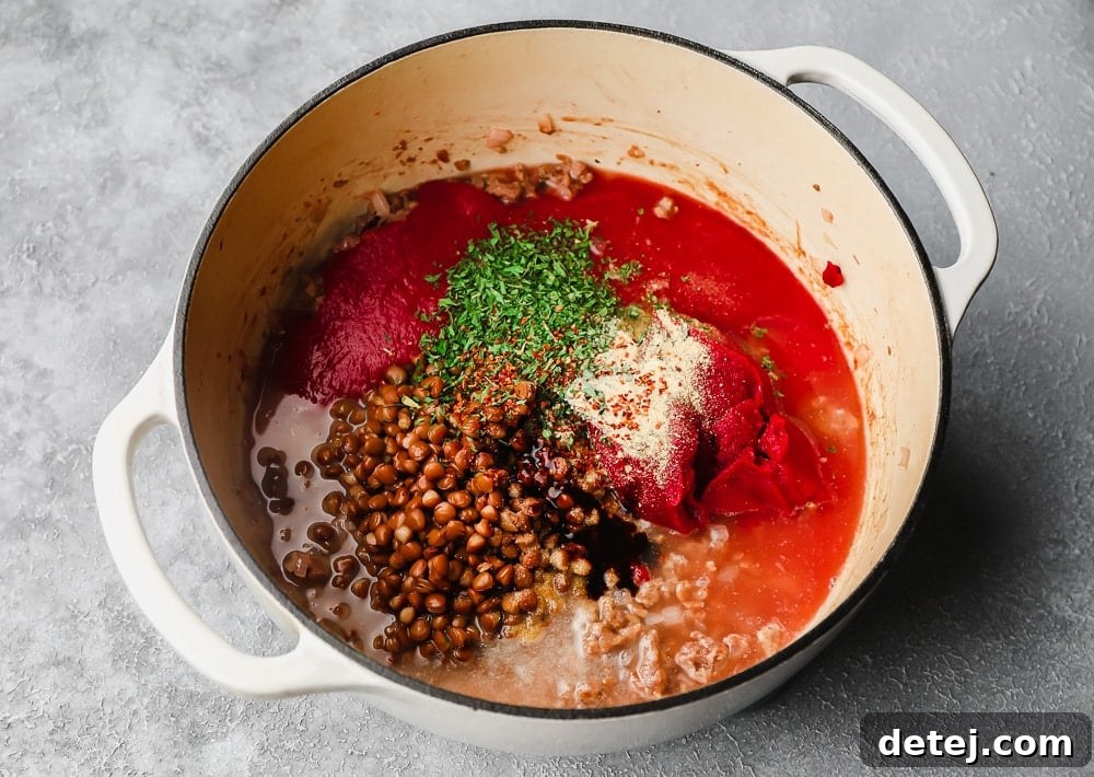 Ultimate Plant-Based Spaghetti 5 Lentils, tomato sauce, and various herbs and spices simmering together in a large white pot, creating a rich red sauce.