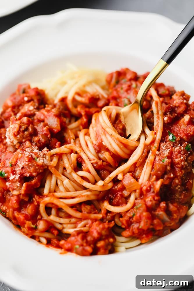 Ultimate Plant-Based Spaghetti 8 A gold fork twirling perfectly coated tomato sauce-covered spaghetti noodles in a white bowl, ready to eat.