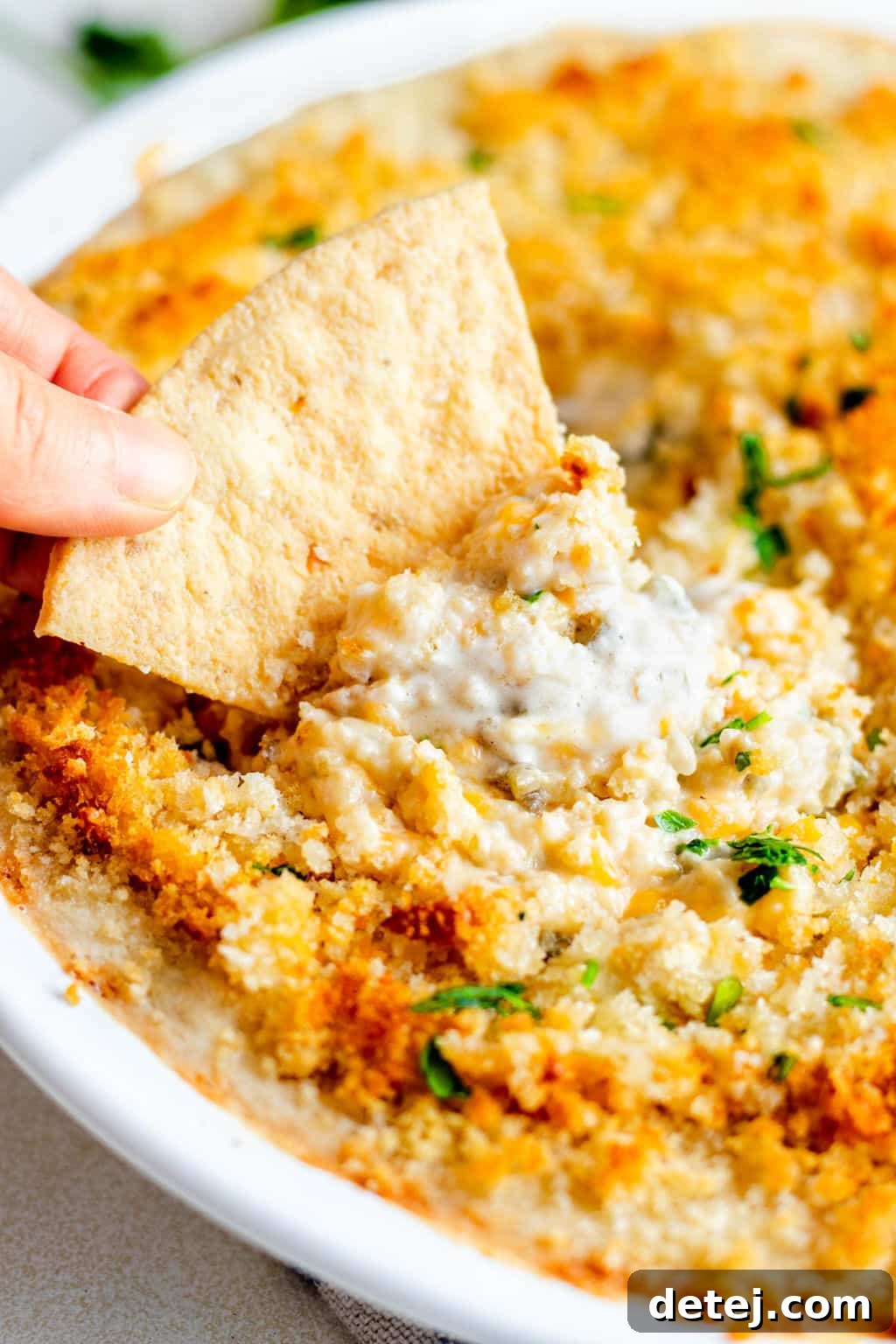 dipping a tortilla chip into a baked white dip.