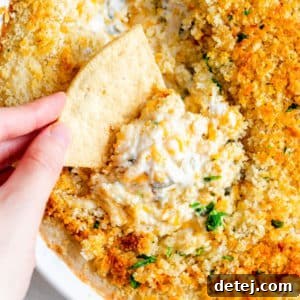 womans hand dipping a tortilla chip into a baked breadcrumb-covered white dip.