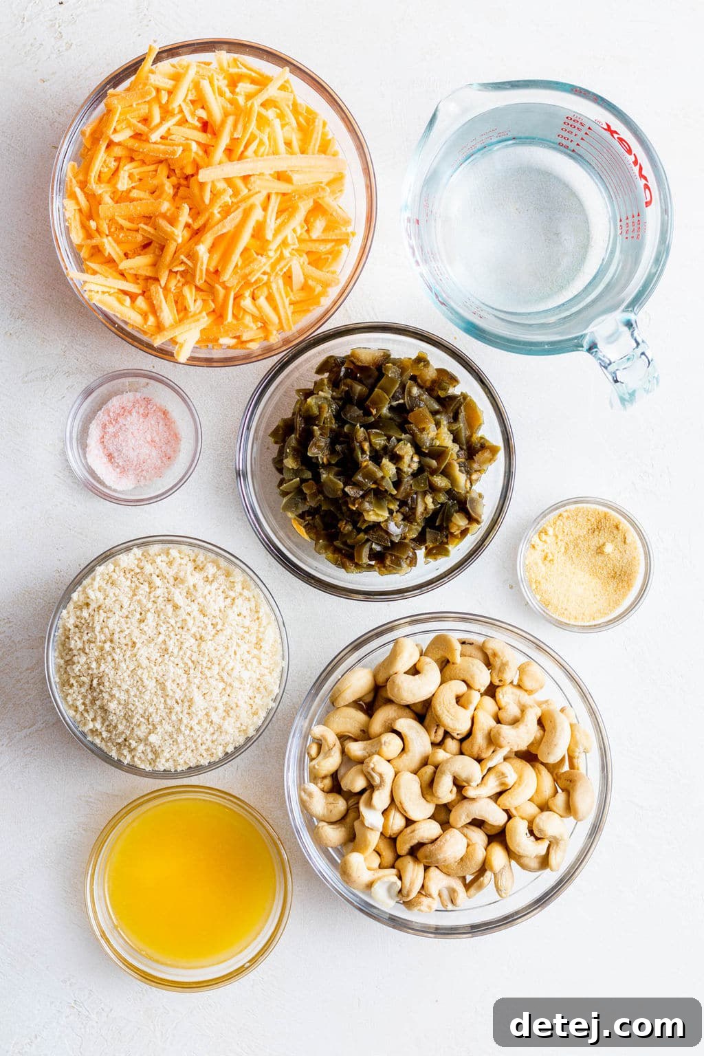 individual glass bowls holding vegan cheddar cheese, jalapeños, breadcrumbs, cashews, and melted butter.