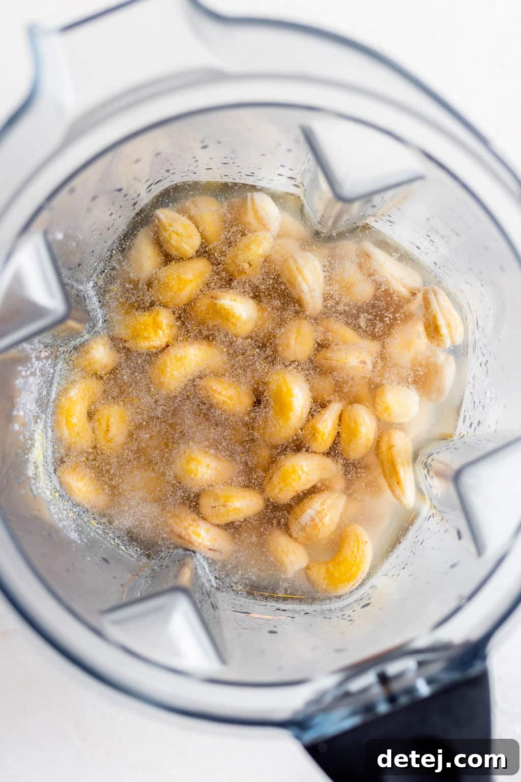 overhead view of cashews and clear liquid in a blender.
