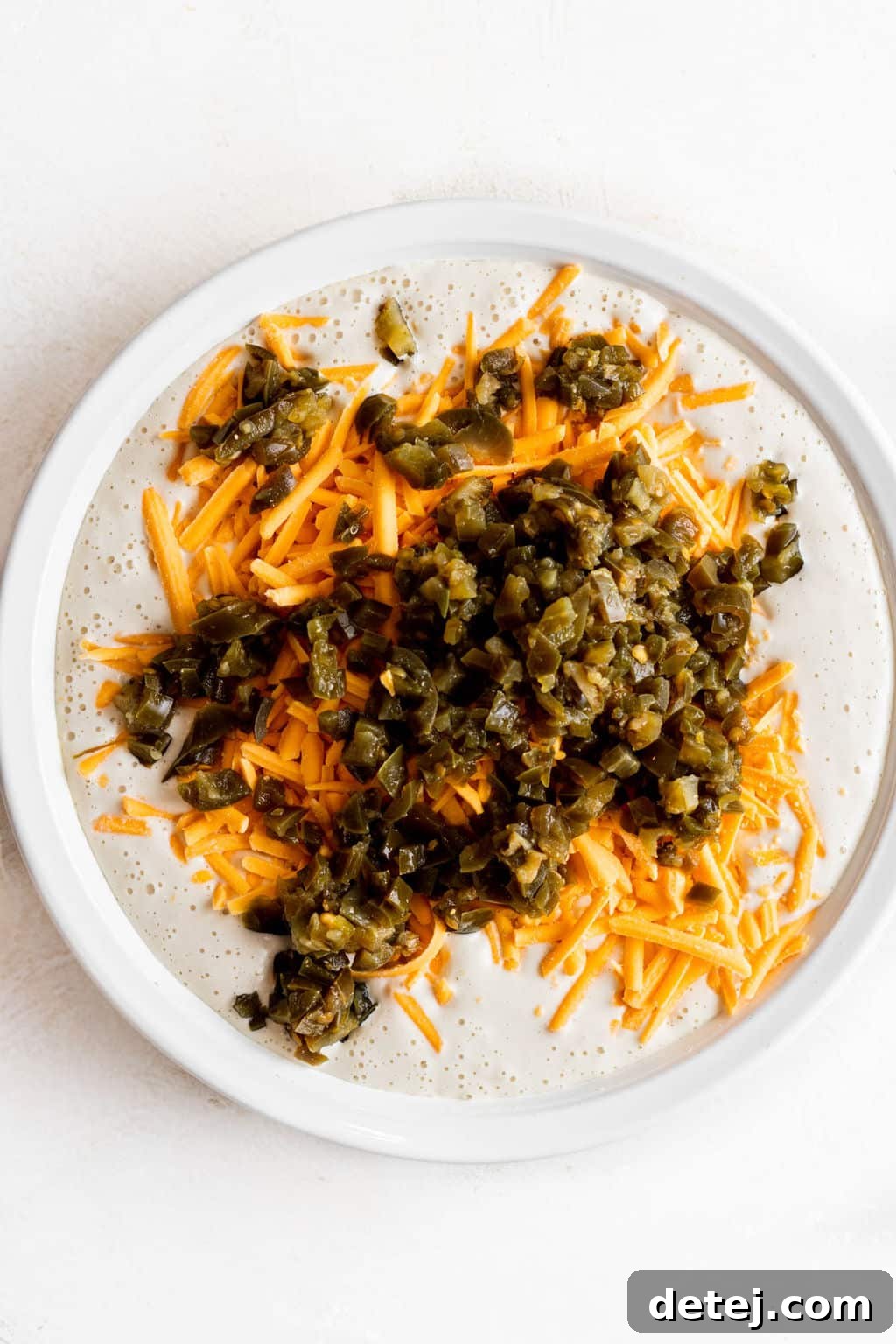 shredded cheddar cheese and diced jalapenos on top of a white liquid.