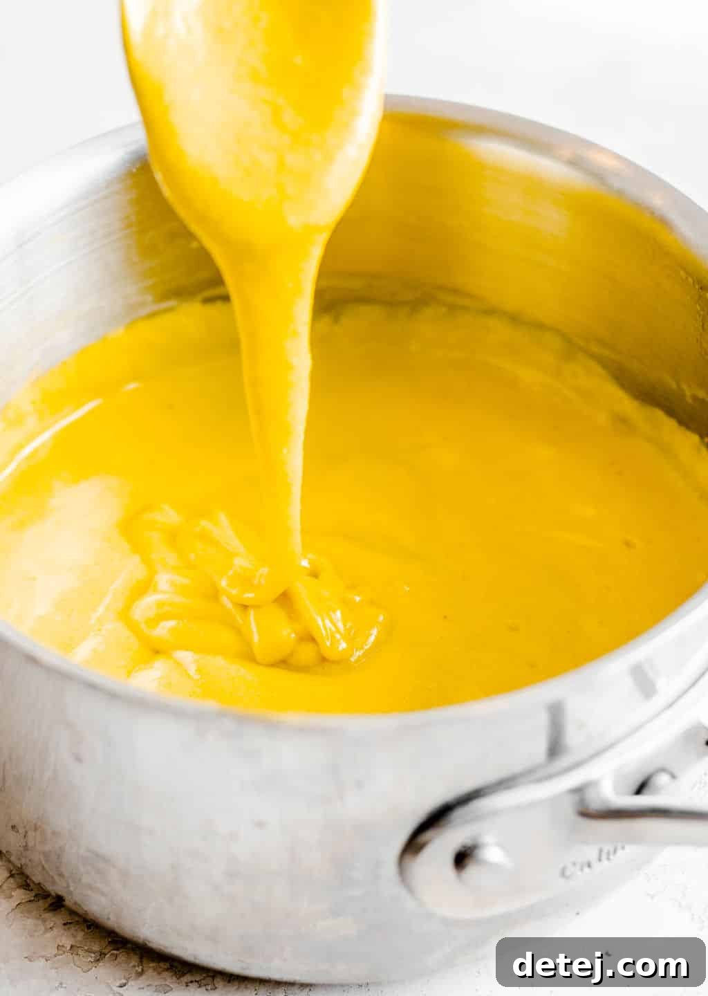A stream of vibrant yellow vegan cheese sauce dripping from a spoon back into a metal pot, showcasing its creamy texture.