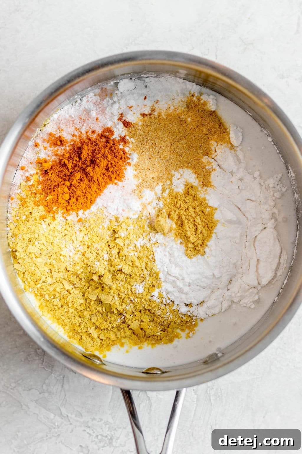 Yellow and white seasonings mixed in a metal pot, ready for whisking.