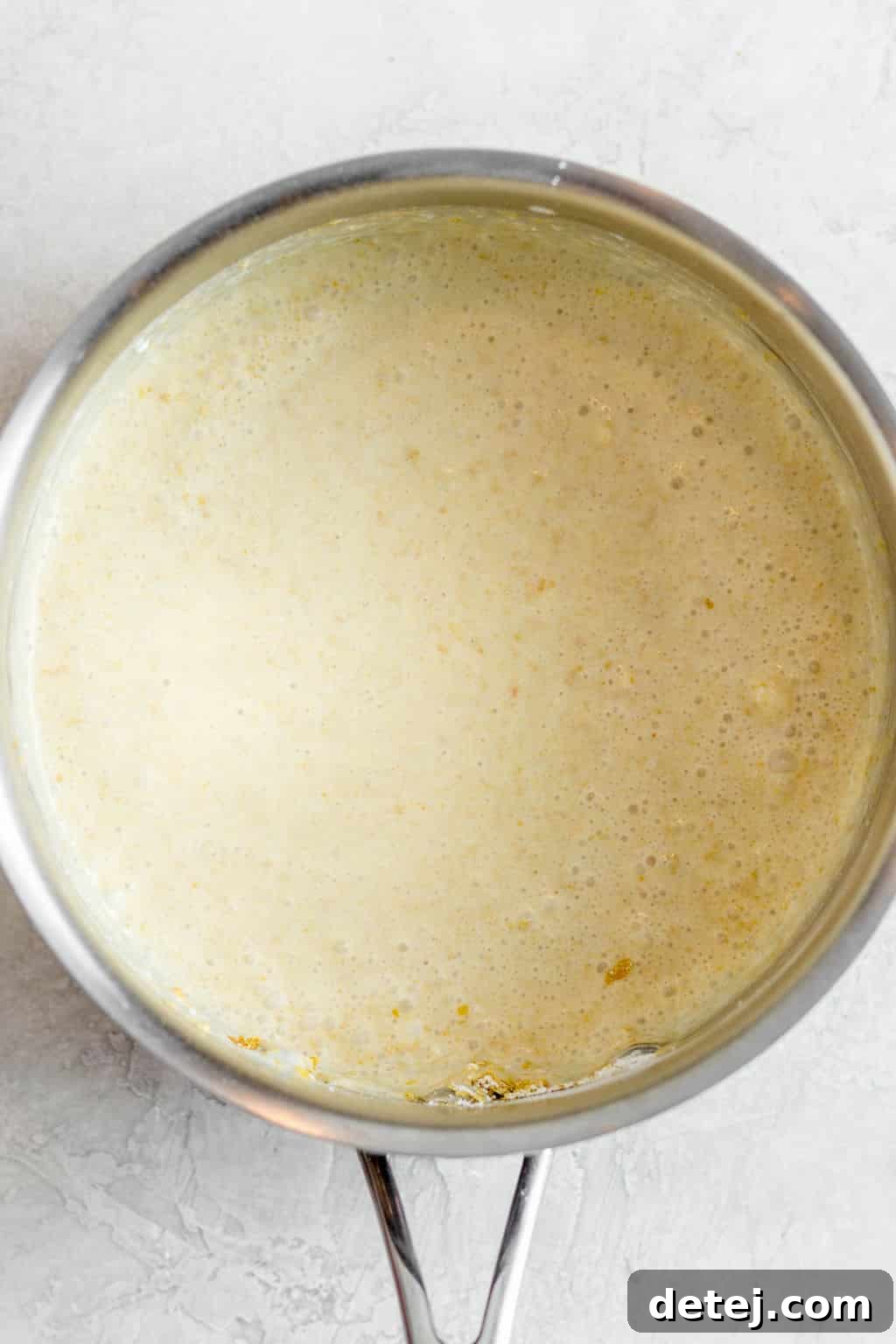 A white, bubbly liquid cooking and thickening in a metal pot over heat.