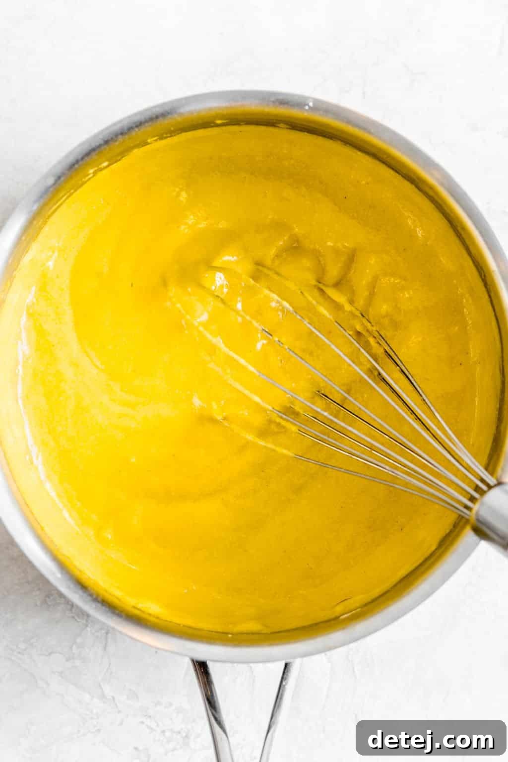 Whisking an orange-hued, creamy vegan cheese sauce in a metal pot, showing its smooth texture.