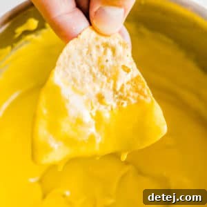 Woman's hand dipping a nacho chip into a pot filled with yellow cheese sauce.
