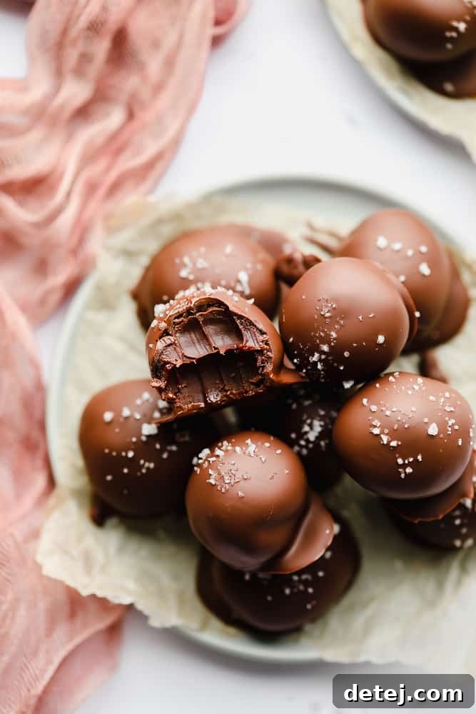 A beautifully arranged pile of homemade vegan chocolate truffles, with one truffle showing a bite taken out, revealing its smooth, dark interior.