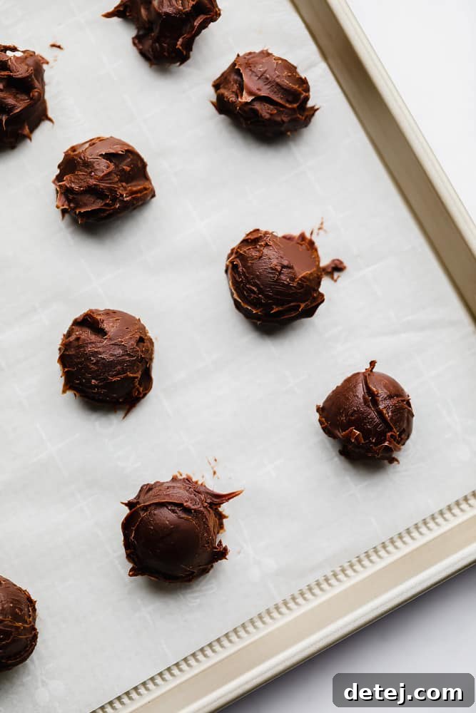 Uniformly portioned chocolate balls arranged neatly on a parchment-lined metal baking sheet, ready for their first chill.