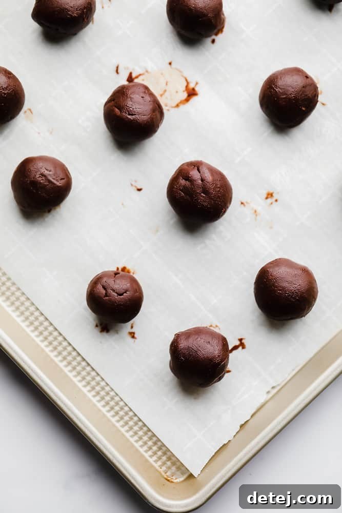 Smooth, perfectly rolled chocolate truffle balls glistening on a parchment-lined metal baking sheet, awaiting their final coating.