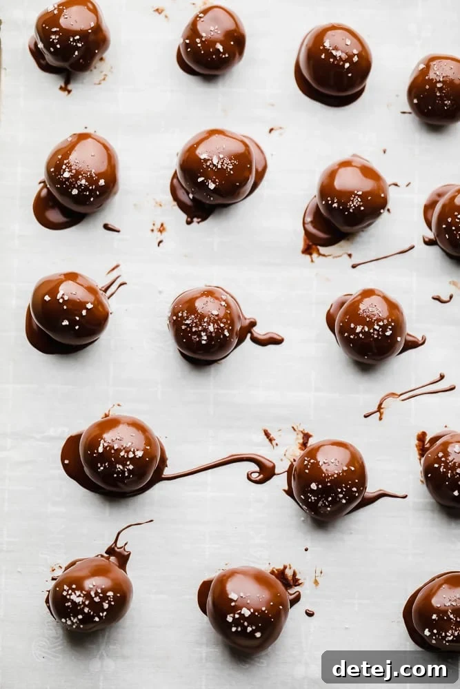 Rows of freshly coated chocolate truffles, some plain and some with toppings, arranged on a parchment-lined baking sheet, chilling to set.