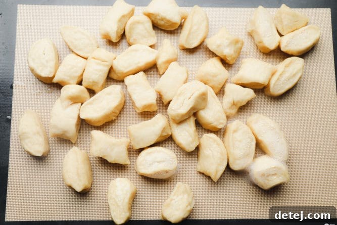 Boiled dough pieces cooling on a silicone mat after being removed from the baking soda bath.