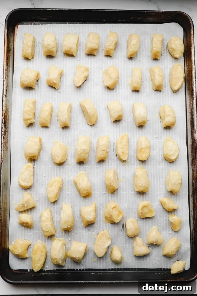 Unbaked pretzel pieces, after the baking soda bath and brushing with butter, ready for salting and baking on a parchment-lined sheet.
