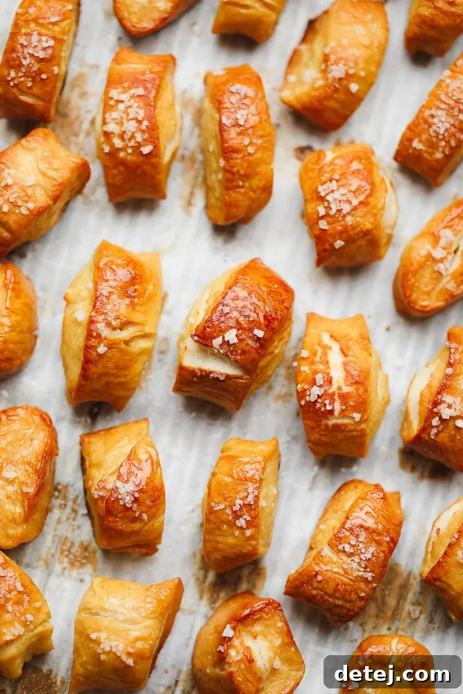 A baking pan filled with numerous baked golden small vegan pretzel bites, generously topped with coarse salt.