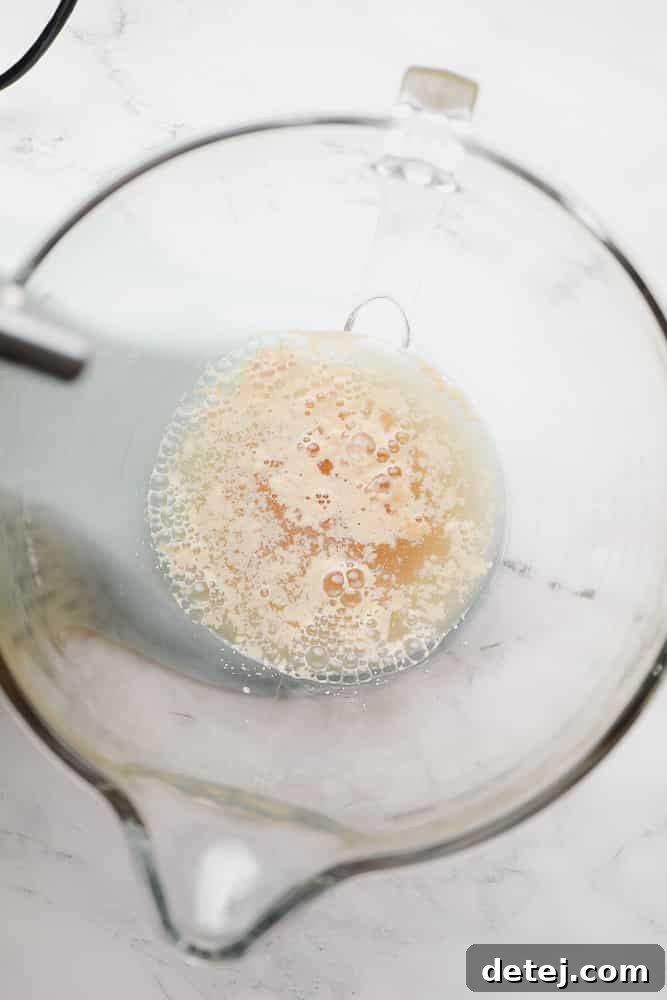 Warm water, brown sugar, and instant yeast mixture showing active bubbling in a glass mixing bowl.