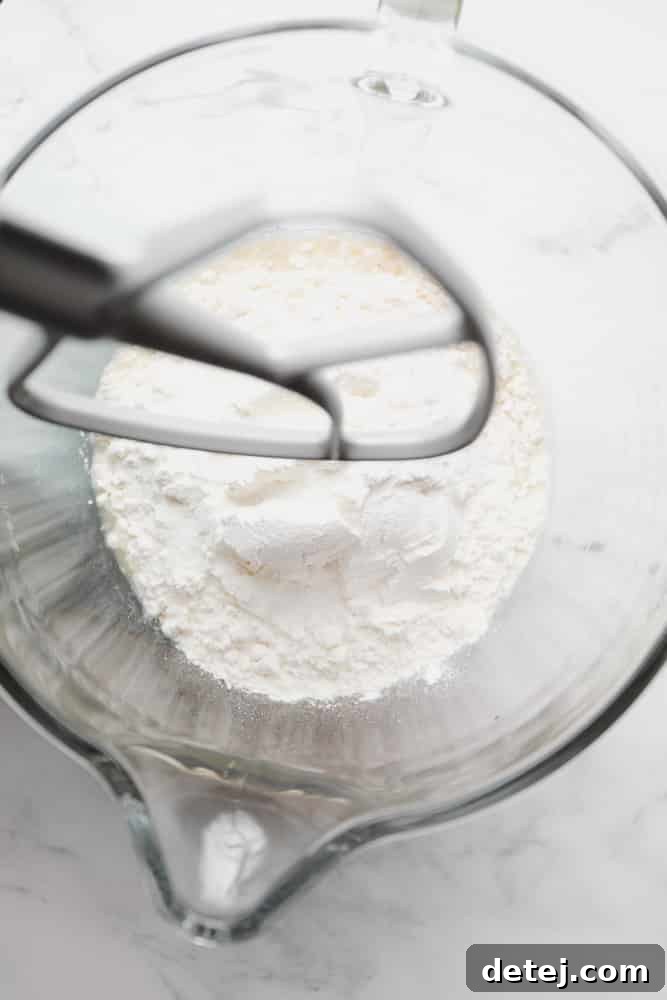 All-purpose flour added to a glass mixing bowl, ready to be combined with the yeast mixture.
